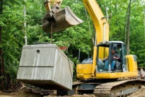an excavator is holding the concrete structure of septic system preparing to lower in place