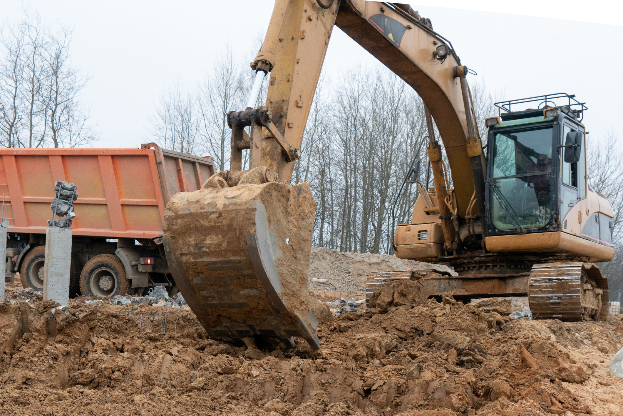 Photograph of an excavator loads a truck with construction sand. Photograph of an excavation site being prepped for septic tank installation