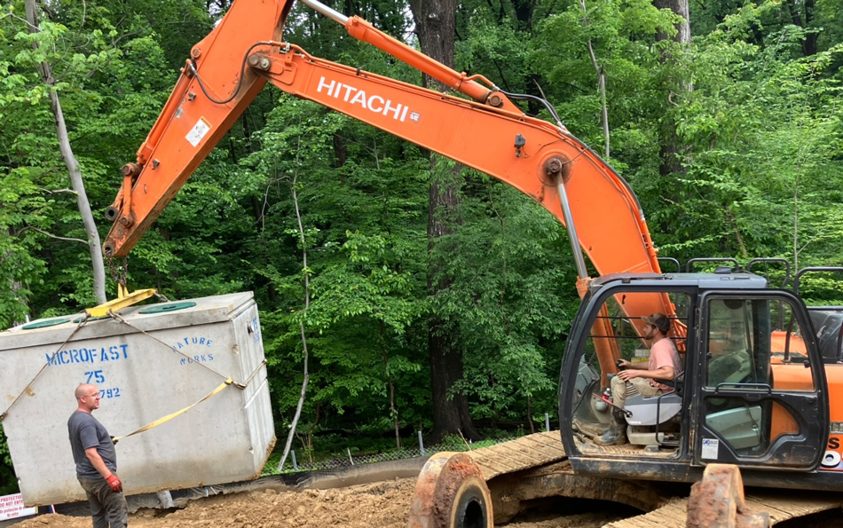 Orange-backhoe-lifting-septic-tank Orange backhoe lifting septic tank